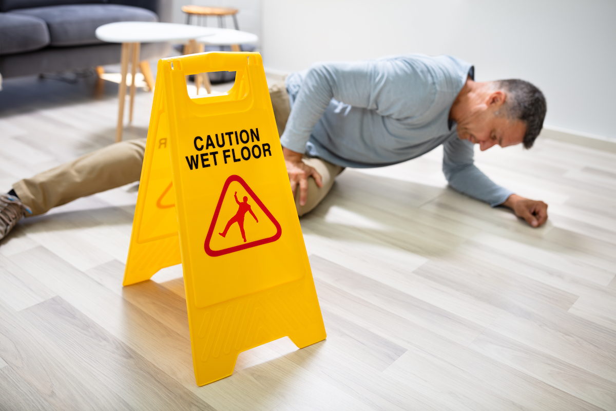 Man Falling On Wet Floor In Front Of Caution Sign